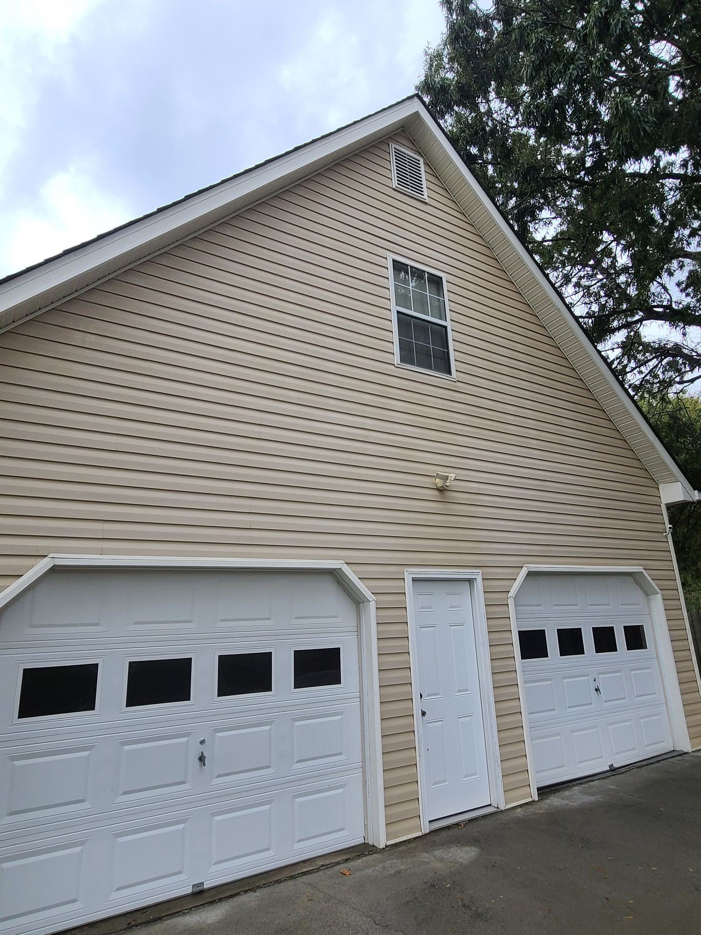 Exterior view of a beige house with two white garage doors and a white entry door.