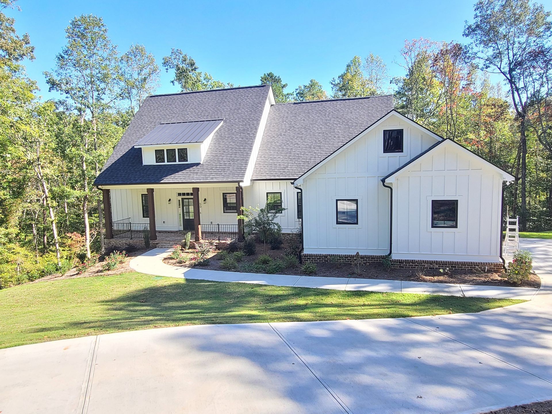 White modern farmhouse with black roof surrounded by trees and a curved driveway.