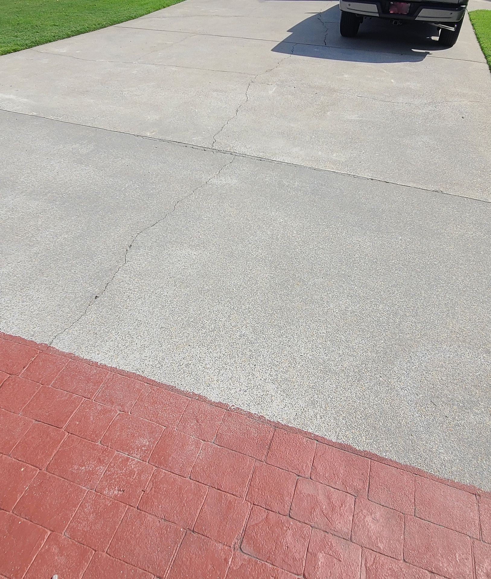 Concrete driveway with visible cracks next to a red brick path and parked vehicle.